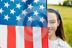 Pretty young pre-teen girl in field holding American flag.