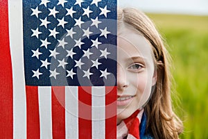 Pretty young pre-teen girl in field holding American flag.