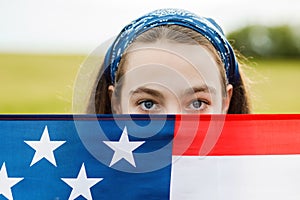 Pretty young pre-teen girl in field holding American flag.