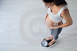 Pretty young pregnant woman standing on scales at home