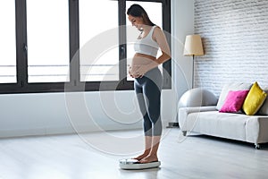 Pretty young pregnant woman standing on scales at home