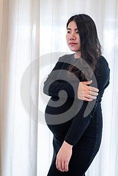 Pretty young pregnant woman standing by the window in room.Concepts of pregnancy and family