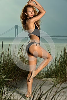 Pretty young woman in black swimsuit posing outdoor in summer on the beach.