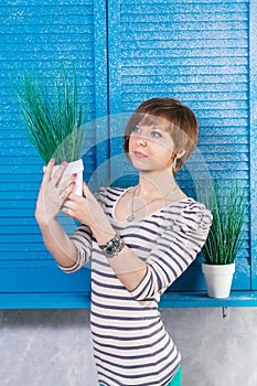 Pretty young short haired caucasian girl holding pott?d plant near blue window. Studio shot, gardening concept, copy space. photo