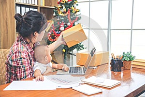 Pretty young single mom working at home on a laptop computer while holding her baby girl sitting on her lap enjoying watching