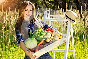 Pretty and young smiling girl keeping wooden box full of vegetables. Summer harvest.