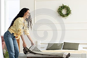 Pretty young smiling lady putting warm plaid on comfy sofa