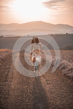 Pekná mladá smilling žena s retro bicykli v západe slnka na ceste, vintage staré časy, dievča v retro štýle na lúke