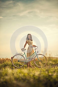 Pretty young smilling woman with retro bicycle in sunset on the road, vintage old times, girl in retro style on meadow