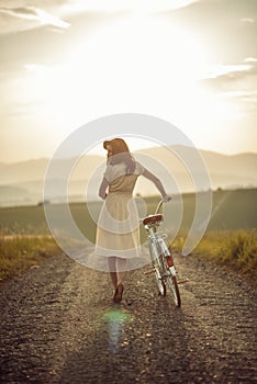 Pretty young smilling woman with retro bicycle in sunset on the road, vintage old times, girl in retro style on meadow