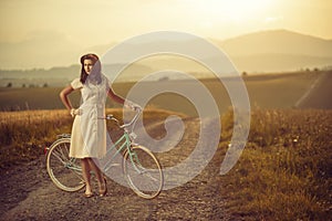 Pretty young smilling woman with retro bicycle in sunset on the road, vintage old times, girl in retro style on meadow