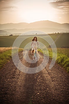 Pekná mladá smilling žena s retro bicykli v západe slnka na ceste, vintage staré časy, dievča v retro štýle na lúke