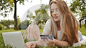 Pretty young student girl makes purchases online using a credit card and laptop computer.