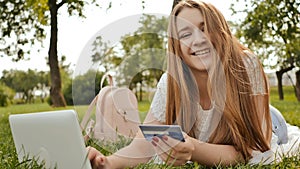 Pretty young student girl makes purchases online using a credit card and laptop computer.