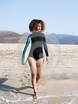 Pretty young surfer female with afro hair walking to the water with her surfboard