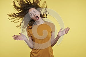 Pretty young surprised woman with curly flying hair, she happy of something, cant belive, isolated over yellow