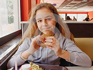 Pretty young teen girl with an appetite eating a hamburger in a cafe