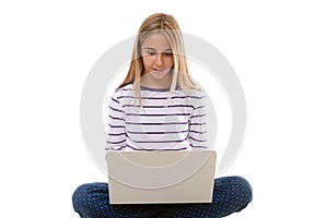 Pretty young teen girl sitting on the floor with crossed legs and using laptop, isolated