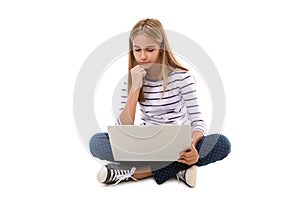 Pretty young teen girl sitting on the floor with crossed legs and using laptop, isolated