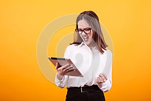 Pretty young teenager can`t contain her happines and holding a tablet in studio over yellow backgroud