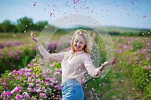 Pretty Young tender woman walking in the tea roses field. Blond lady wearing jeans and retro hat enjoy summer day