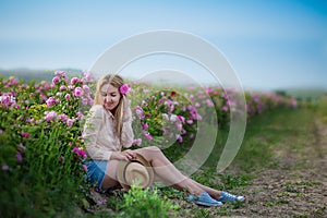 Pretty Young tender woman walking in the tea roses field. Blond lady wearing jeans and retro hat enjoy summer day