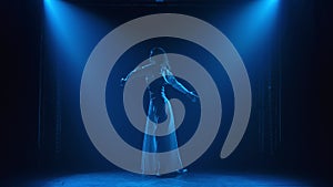 Pretty young woman actress in the image of Joan of Arc is dancing on stage with a sword. Silhouette of a slender body in