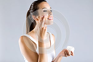 Pretty young woman applying body cream. Isolated on gray background.