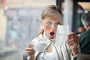 Pretty, young woman baffled with the bill in a coffeeshop