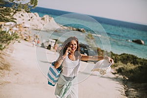 Pretty young woman with a bag using mobile phone on the beach