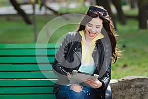 Pretty young woman with beautiful smile using tablet in the park at the sunset.