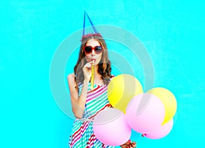 Pretty young woman in a birthday cap blowing a whistle holds an air colorful balloons