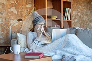 Pretty young woman blowing her nose on the sofa at home with the laptop.