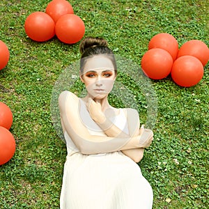 Pretty young woman with bright make up. Outdoor green portrait. Red balloons