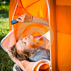 Pretty, young woman camping outdoors, lying in the tent