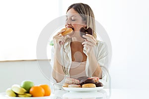 Pretty young woman choosing between fruit and sweet, and finally, choose donuts at home.