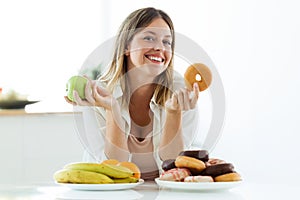 Pretty young woman choosing between fruit and sweet at home.