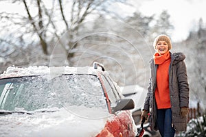 Pretty, young woman cleaning her car from snow