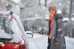 Pretty, young woman cleaning her car from snow after heavy snowstorm