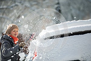 Pretty, young woman cleaning her car from snow after heavy snowstorm