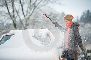Pretty, young woman cleaning her car from snow after heavy snowstorm