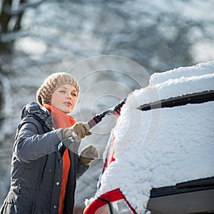 Pretty, young woman cleaning her car from snow after heavy snowstorm