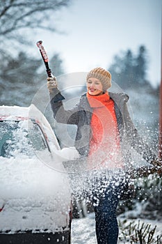 Pretty, young woman cleaning her car from snow