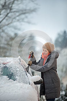 Pretty, young woman cleaning her car from snow after heavy snowstorm