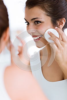 Pretty young woman is cleaning her face while looking in the mirror in the bathroom.