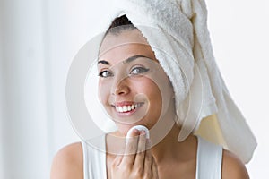 Pretty young woman is cleaning her face while looking in the mirror in the bathroom.