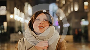 Pretty young woman in a coat and with a scarf is walking in the night city. Walk along the evening streets in the autumn