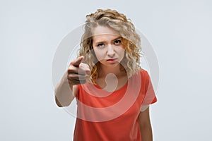 Pretty Young woman with curly hair looking at the camera and pointing her finger at you. Human emotions concept