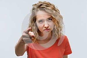 Pretty Young woman with curly hair looking at the camera and pointing her finger at you. Human emotions concept