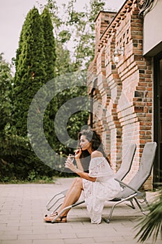 A young woman with curly hair relaxes on a deck chair and enjoys a glass of fresh lemonade